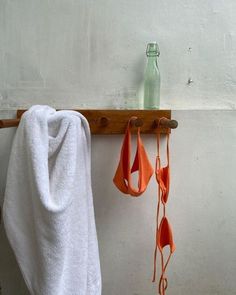 two towels hanging on a wooden rack next to a bottle and towel holder with hooks