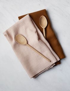 two wooden spoons sitting on top of napkins next to some brown and white cloth