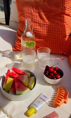 a table topped with fruit and drinks next to a bowl of cherries on top of a white table cloth