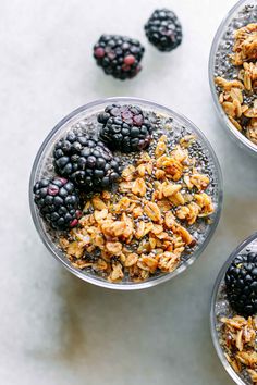 three bowls filled with granola and blackberries on top of a white countertop