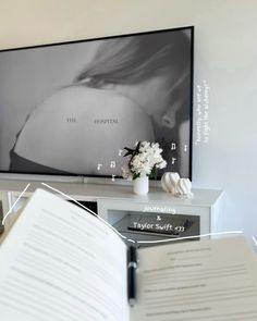 an open book sitting on top of a table next to a tv screen and vase with flowers