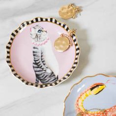 a plate with a cat on it next to a snake and gold charm bracelets