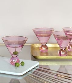 four pink glass goblets sitting on top of a white plate next to a gold tray