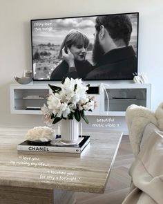 a living room with a large television mounted on the wall and white flowers in a vase