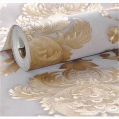 a roll of gold foiled paper on top of a white wallpaper with golden flowers