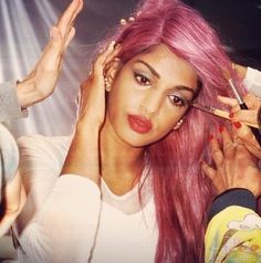 a woman with pink hair getting her makeup done