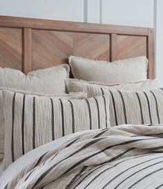 a bed with black and white striped pillows on top of it, next to a wooden headboard