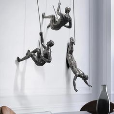three metal sculptures hanging from the side of a white wall next to a table and chair