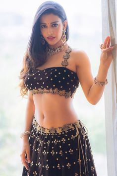 a beautiful young woman in a black and gold outfit standing next to a window with her hand on her hip