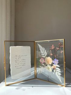 two framed pictures with flowers on them sitting on top of a white tablecloth covered table