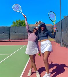 two women standing on a tennis court holding racquets in their hands and posing for the camera