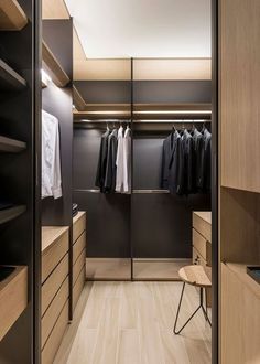 a walk - in closet with clothes hanging on the walls and wooden shelves, along with a stool