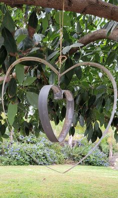 a heart shaped metal object hanging from a tree branch in the middle of a garden