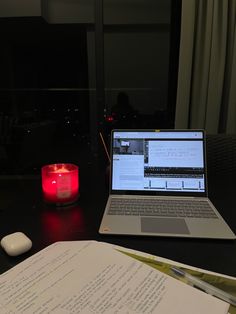 an open laptop computer sitting on top of a desk next to a candle and paper