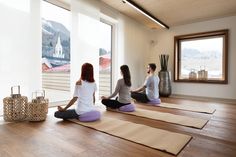 three women are sitting on yoga mats in the middle of a room with large windows
