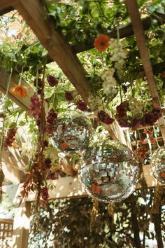 disco ball decorations hanging from a pergolated roof in an outdoor setting with flowers and greenery