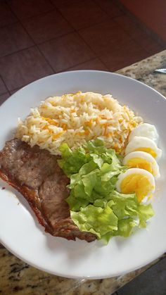 a white plate topped with meat, rice and lettuce next to an egg