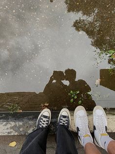 two people standing next to each other in front of a puddle on the ground with their feet up
