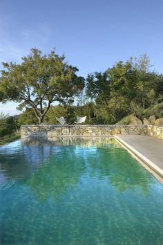 an outdoor swimming pool surrounded by stone walls and green trees in the background with blue sky