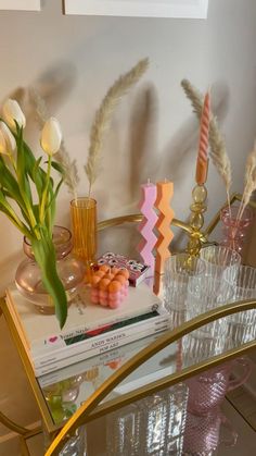 a glass table with flowers, candles and books on it in front of a mirror
