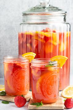 two mason jars filled with lemonade and strawberries next to sliced oranges on a cutting board