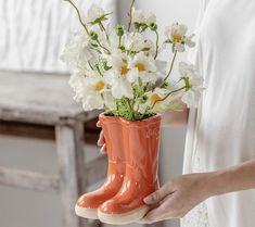 a woman holding a vase with white flowers in it and wearing orange rubber boot boots