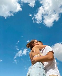 a man and woman kissing in front of a blue sky with white clouds above them