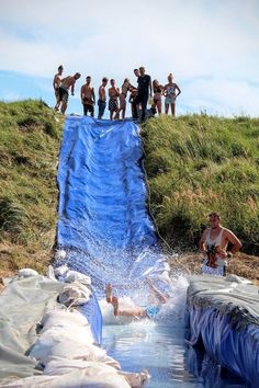 several people are standing on the edge of a water slide while others watch from above