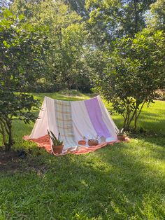 a tent is set up in the middle of some trees and grass with potted plants next to it