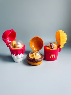 three mcdonald's toys are shown on a gray background, one has an egg shell and the other is a cupcake