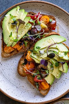 two pieces of bread with avocado and tomatoes on them sitting on a plate
