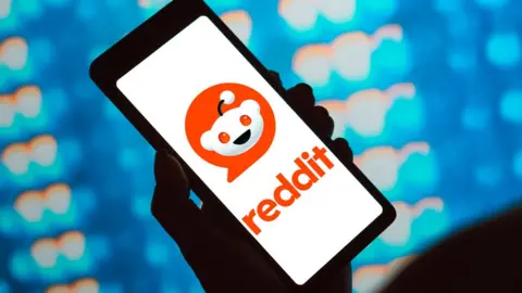 Getty Images A hand holding a phone with the Reddit logo on it