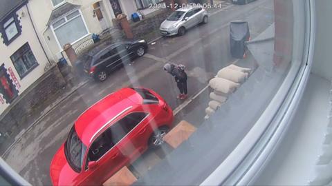 Popescu hunching behind a car on the street in a CCTV image