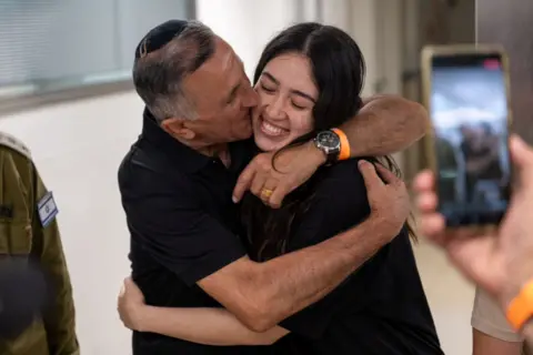 Noa Argamani, a rescued hostage, grins as she embraces and is kissed on the cheek byher father, Yakov Argamani, in a medical centre.