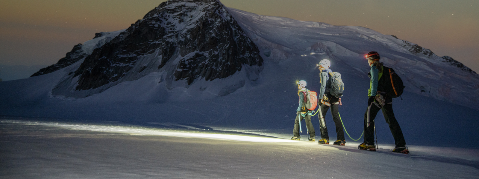 Tres senderistas atraviesan una montaña nevada bajo un cielo estrellado