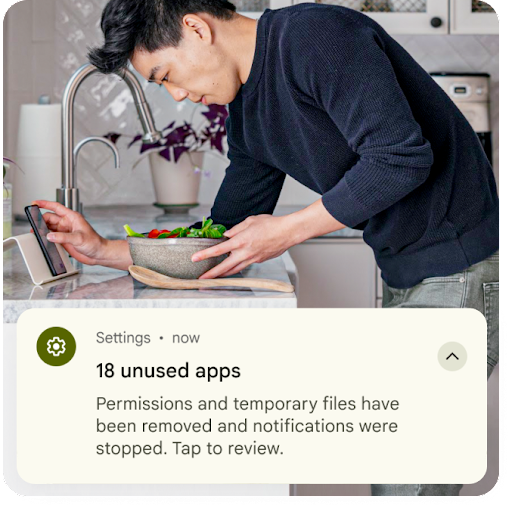 Mutfakta yemek hazırlarken Android telefonuna bakan bir kişinin resmi. Resmin üzerindeki grafikte ayarlar bildirimi gösteriliyor. Bildirimde, kullanılmayan uygulamalara ait geçici dosyaların kaldırıldığı ve izinlerin sıfırlandığı yazıyor.