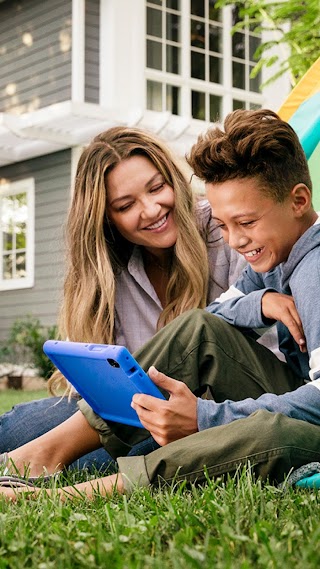 Mother and son both using a tablet while camping in their backyard.