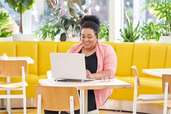 Une femme souriante assise à une table de café, face à son ordinateur portable.