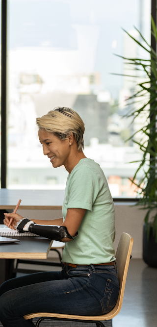 Ofiste oturup dizüstü bilgisayarında çalışan protez kollu bir kadın.
