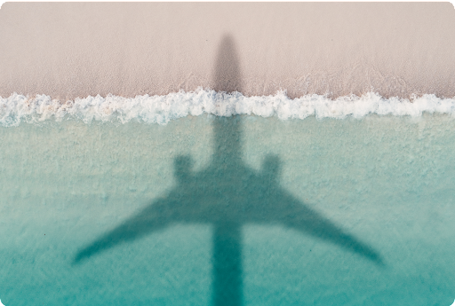 Vista aérea de la sombra de un avión sobre las olas en una costa.