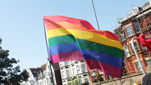 A rainbow Pride flag waves in the wind, carried down a street in a parade.