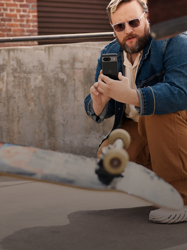 En Android-bruker står på huk og tar opp en video av en skateboarder som gjør et triks.
