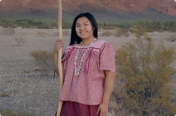 Una joven indígena con una blusa y una falda rosadas parada en la Reserva de la Nación Tohono O'odham