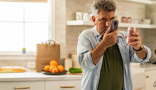 Seorang laki-laki yang berdiri di dapur sedang menggunakan ponsel Androidnya untuk membaca label kaleng.
