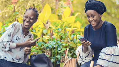 Dos mujeres afrodescendientes con vestidos coloridos sostienen teléfonos inteligentes y sonríen