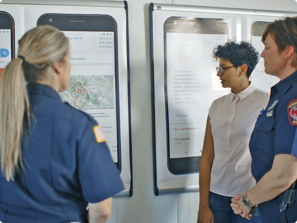 A Googler and three first responders stand in front of posters displaying examples of how a wildfire boundary map appears on Google Search.