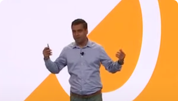 Un hombre con una camisa gris hace un gesto expresivo mientras se presenta en el escenario
