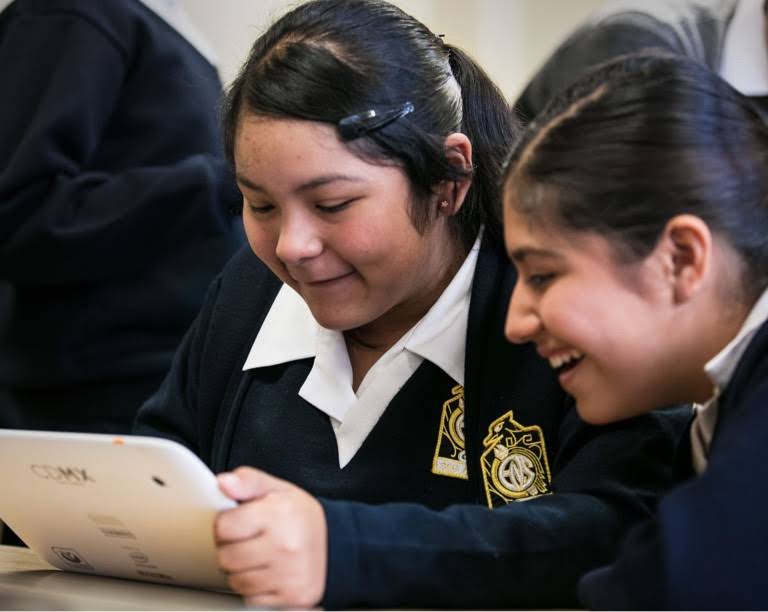 교복을 입고 미소 짓는 두 명의 여학생 중 태블릿 기기를 들고 있는 한 학생
