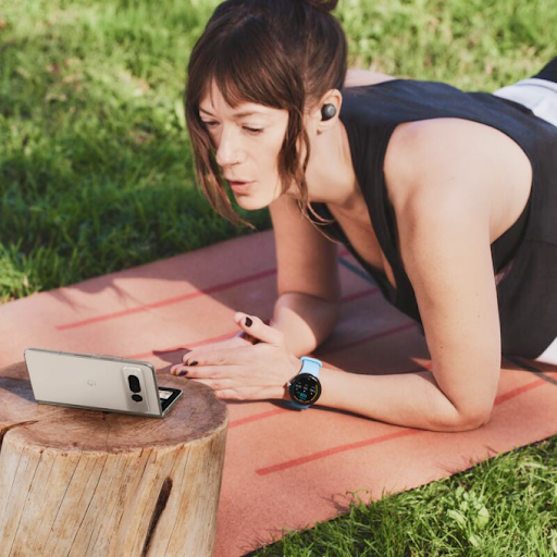 Une personne qui porte une montre connectée Wear OS et des écouteurs s'entraîne sur un tapis de yoga tout en regardant un téléphone Android pliable.