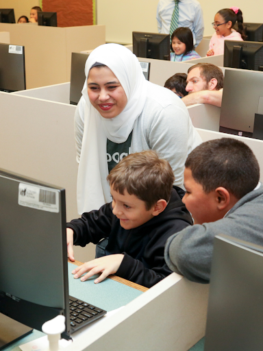 Profesora en un hiyab sonríe a dos jóvenes estudiantes varones en la computadora